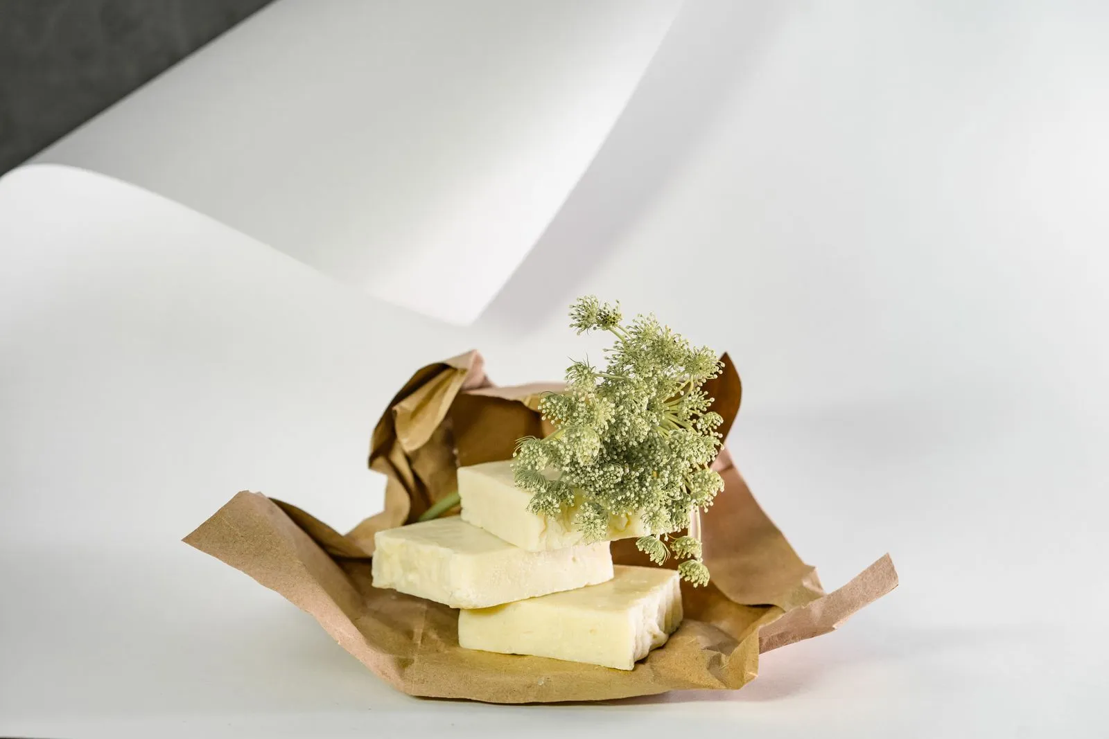 Aesthetic arrangement of natural soap bars with delicate white flowers on kraft paper and neutral background.